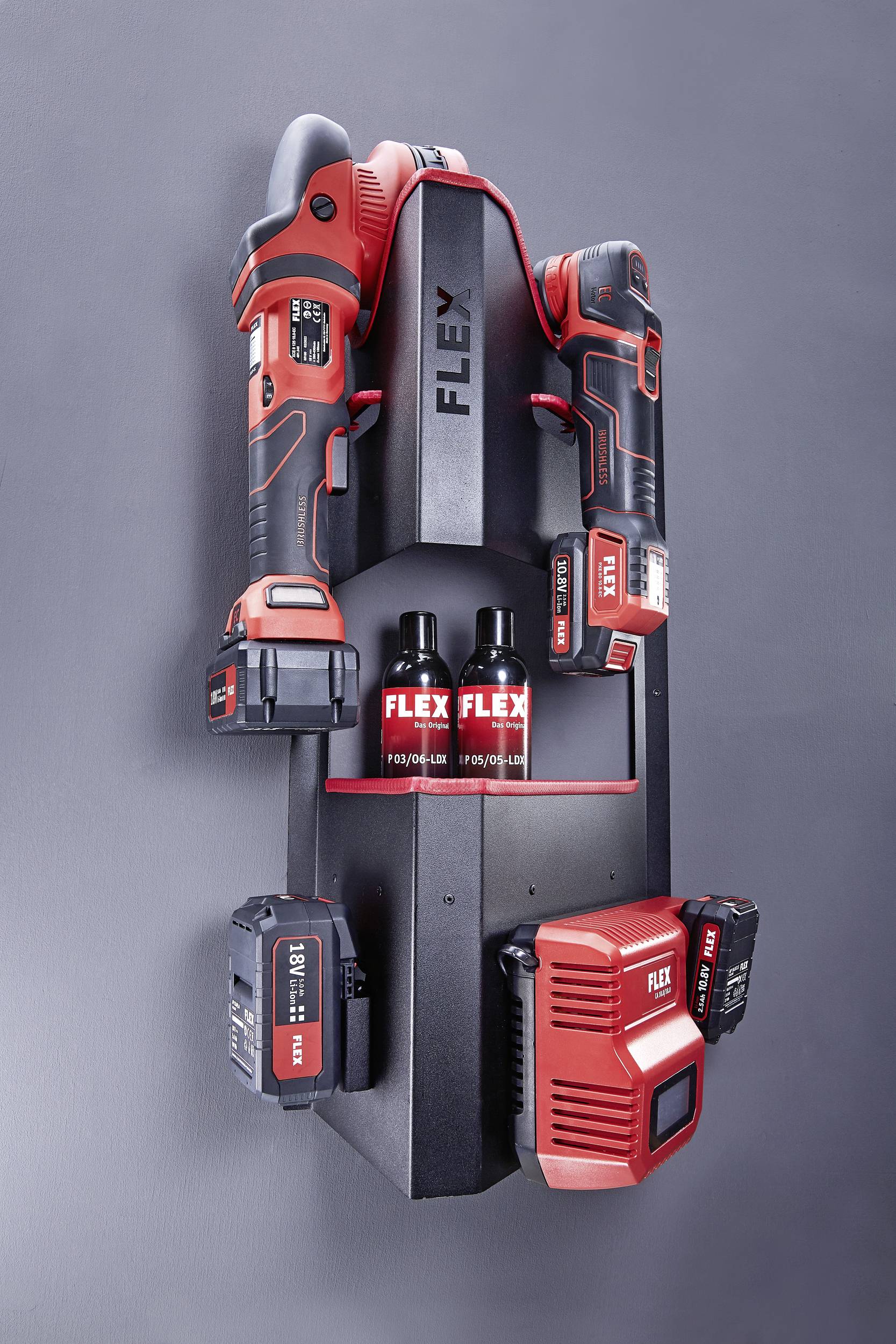 Tool wall mount with two red cordless drills, three batteries and a charger, marked with 'Flex'. Functional arrangement.