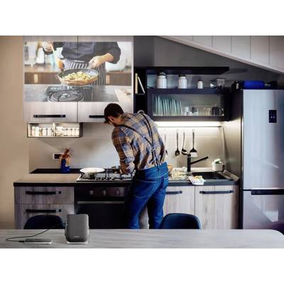 A man is cooking in a modern kitchen, with a cooking recipe video projected onto a screen in the background.
