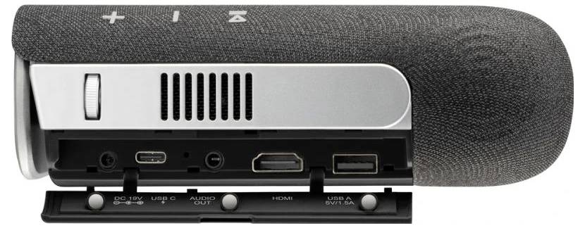 A portable speaker with a grey fabric cover and a silver strip. On the strip are connections for HDMI, USB and audio.