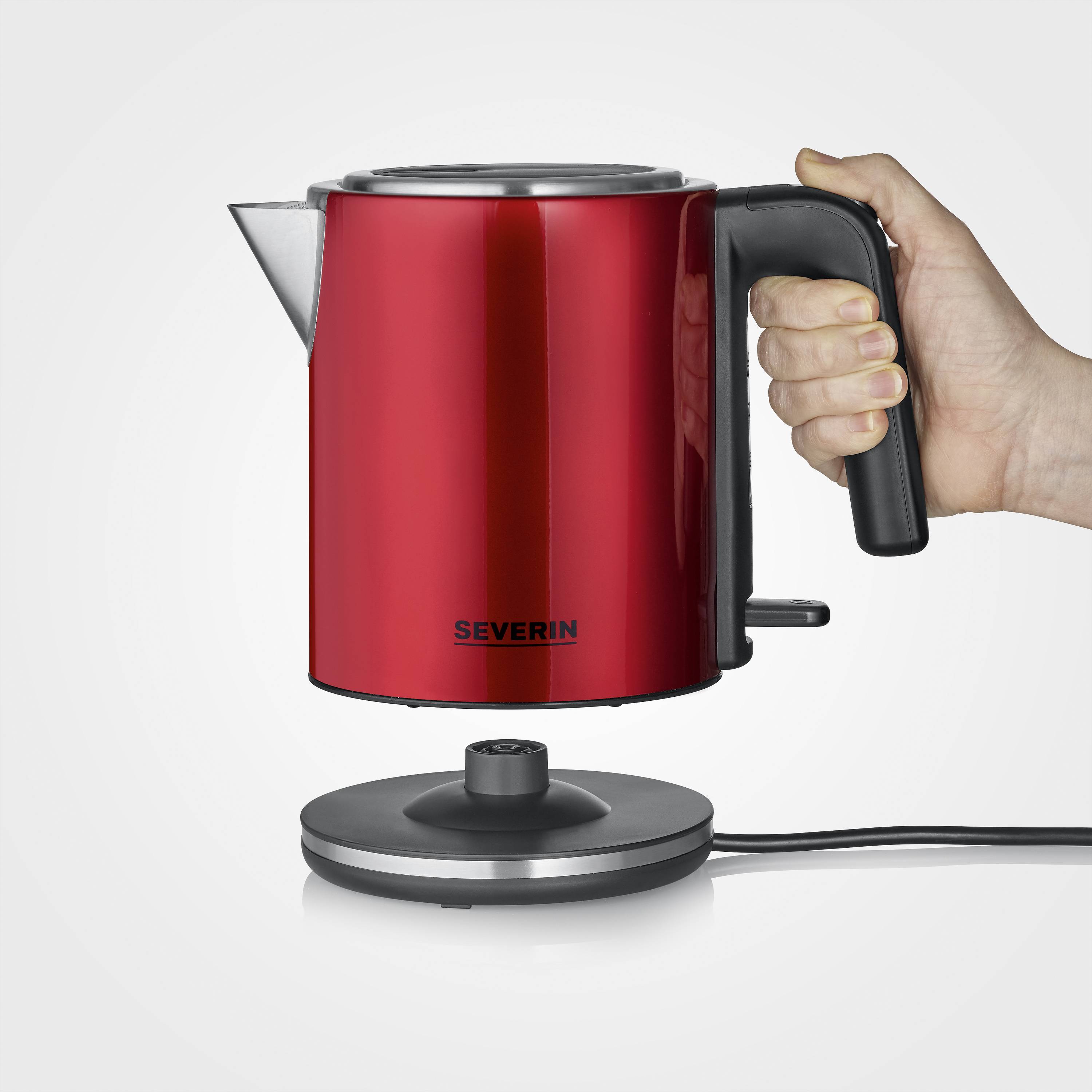 Red kettle in a stylish design, cordless with a removable base. One hand lifts the kettle, demonstrating easy handling.