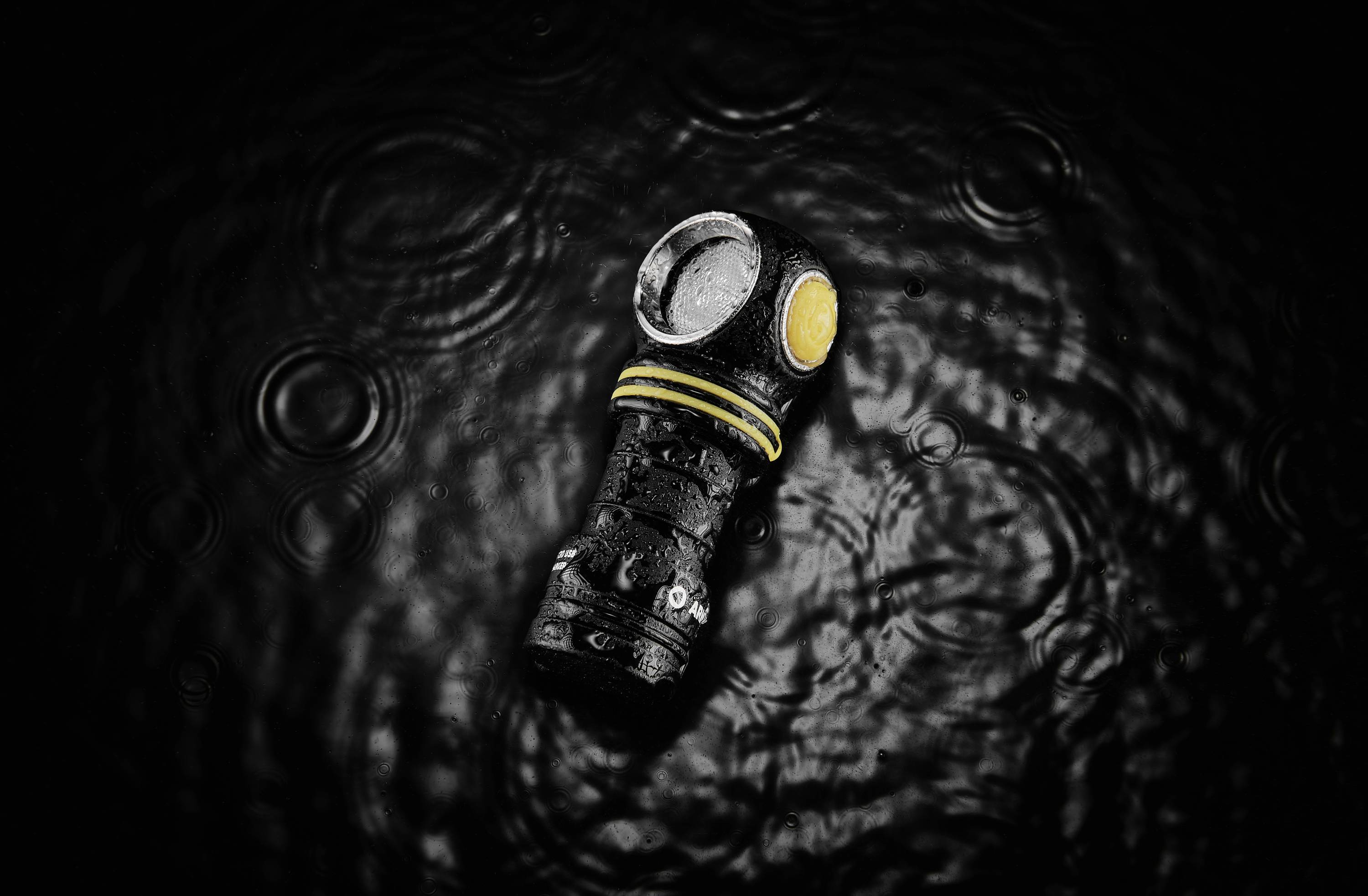 'Torch with yellow button in black water, water droplets on it, surrounded by concentric waves.'
