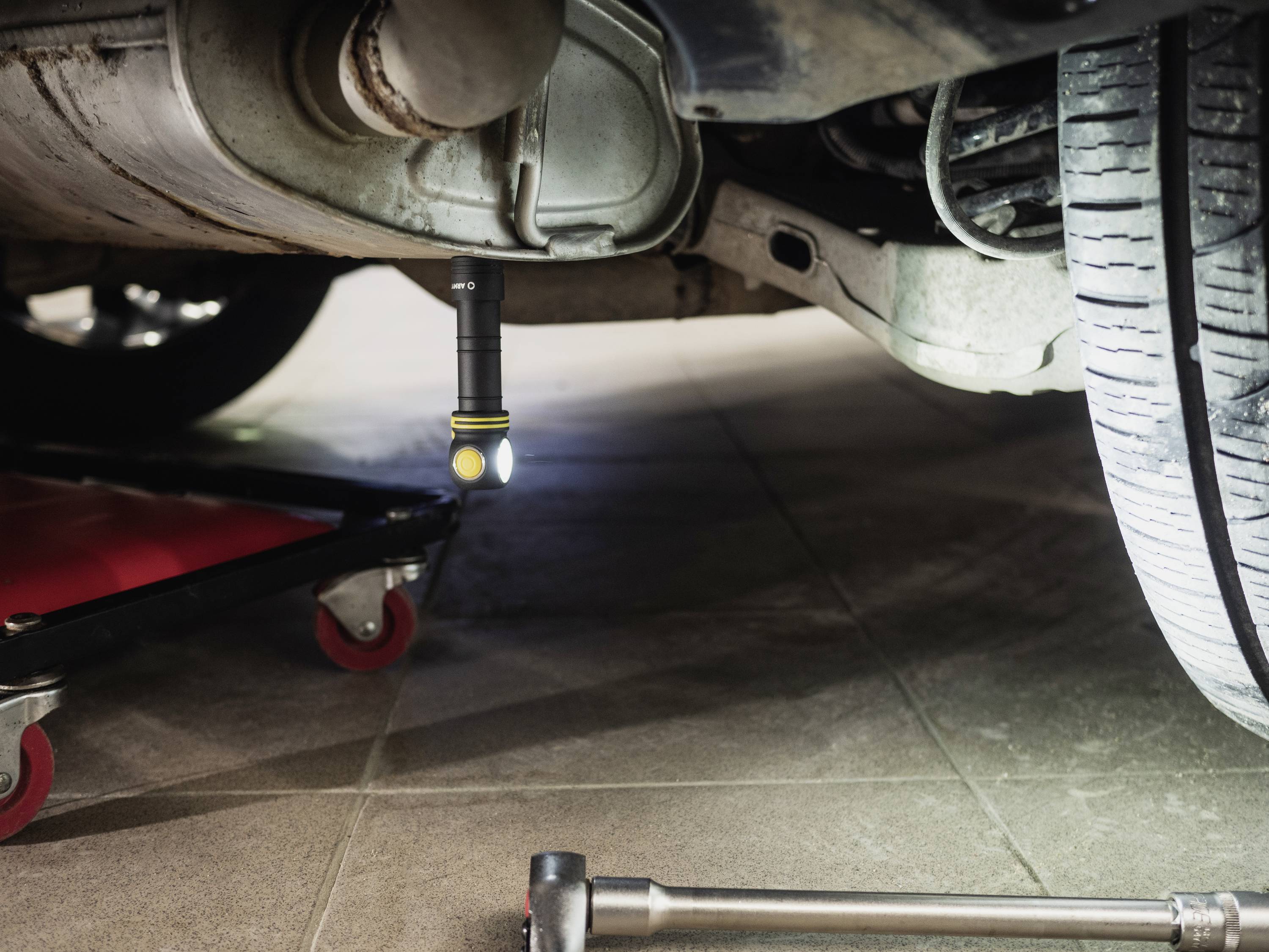 View underneath a car with a torch shining light on the exhaust pipe. A tool and trolley jack are also visible.