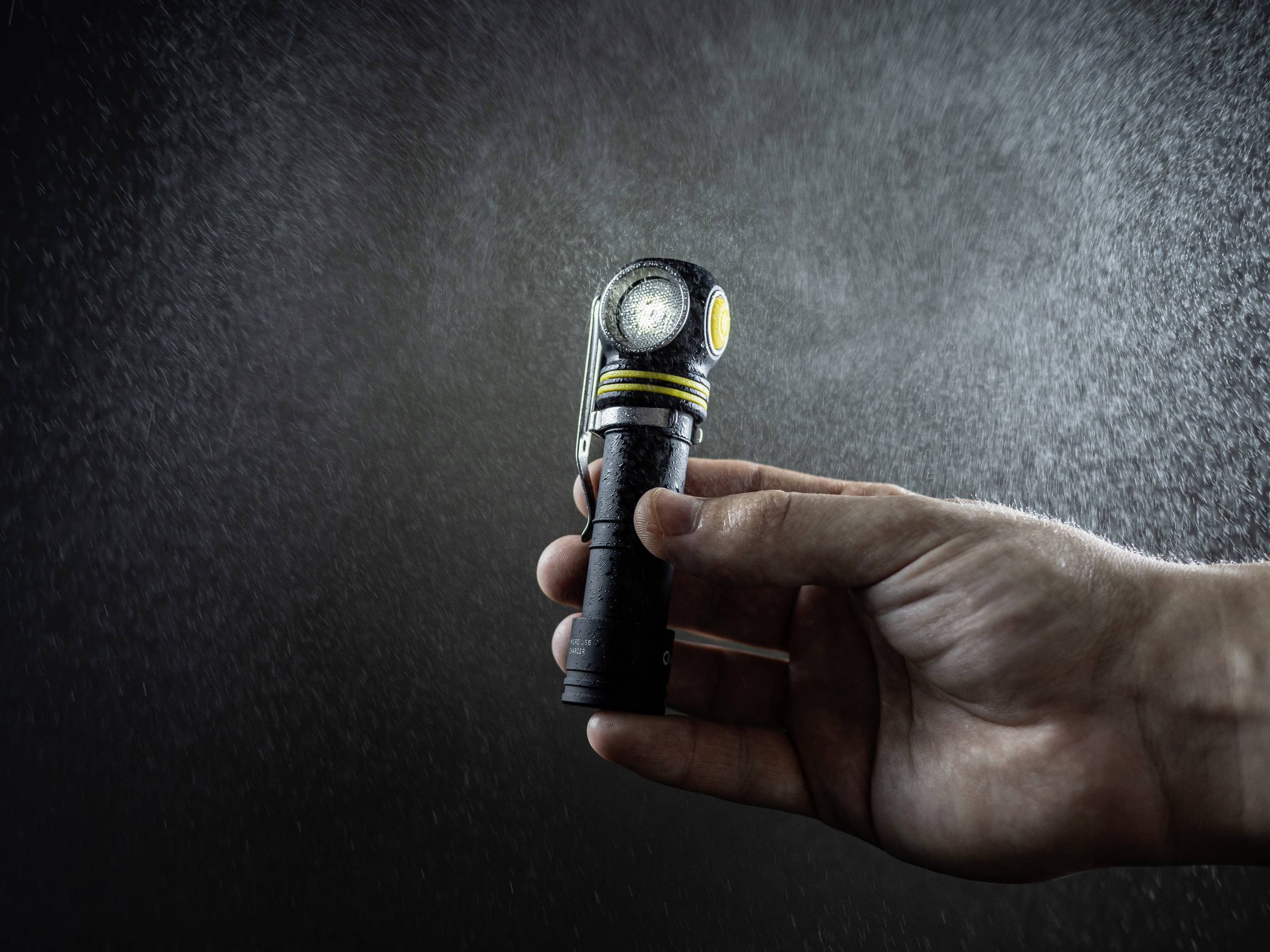 A hand holds a torch in a dark room. The torch is illuminated, creating a beam that lights up fine particles in the air.