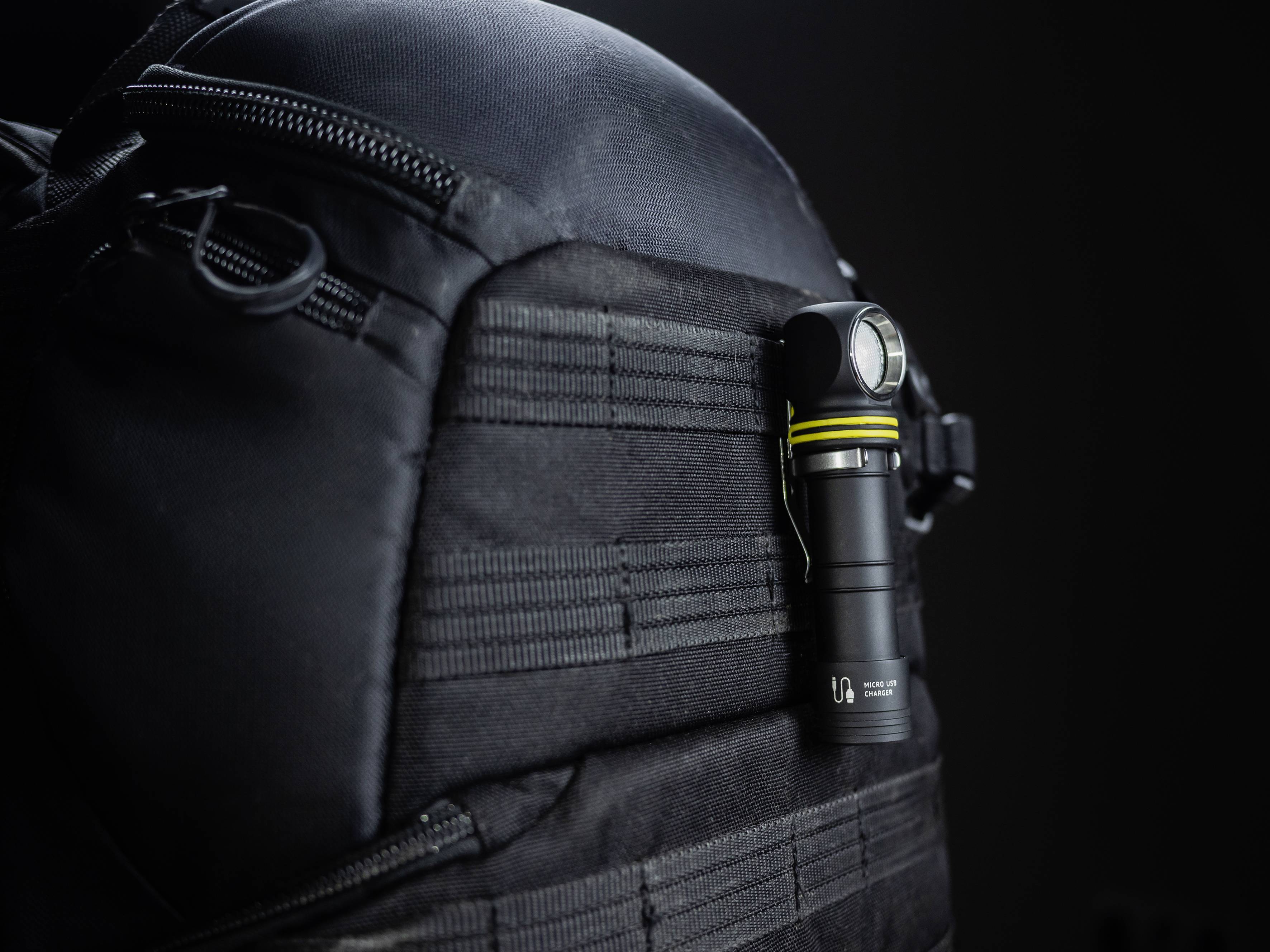 A torch is attached to a black rucksack. The scene is captured against a dark background, which emphasises the torch.