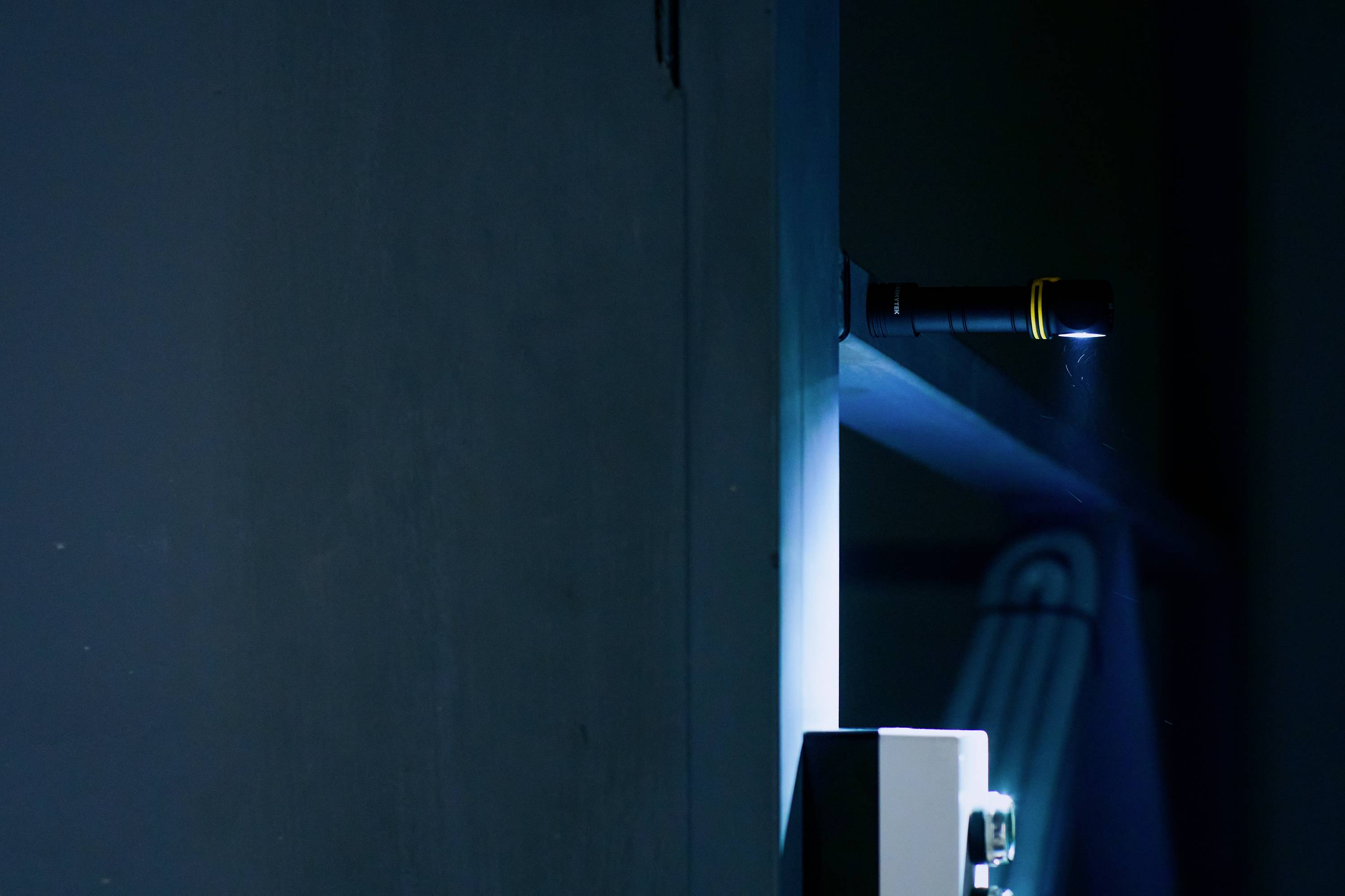 A torch illuminates the dark blue space from the side, casting light on a corner with an electrical control box and a ladder in the background.