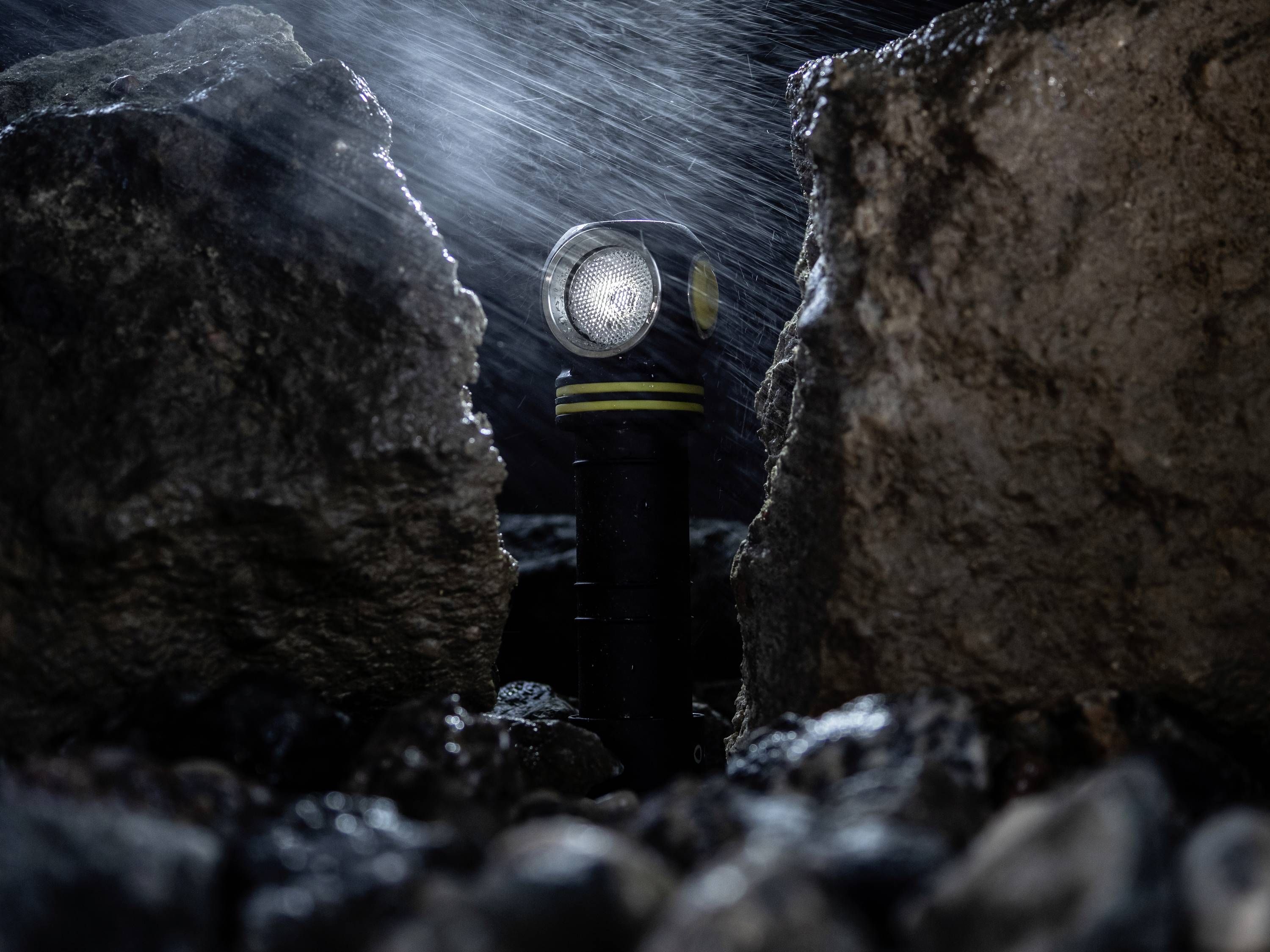 Torch with a bright beam standing between wet stones in a rainy environment.