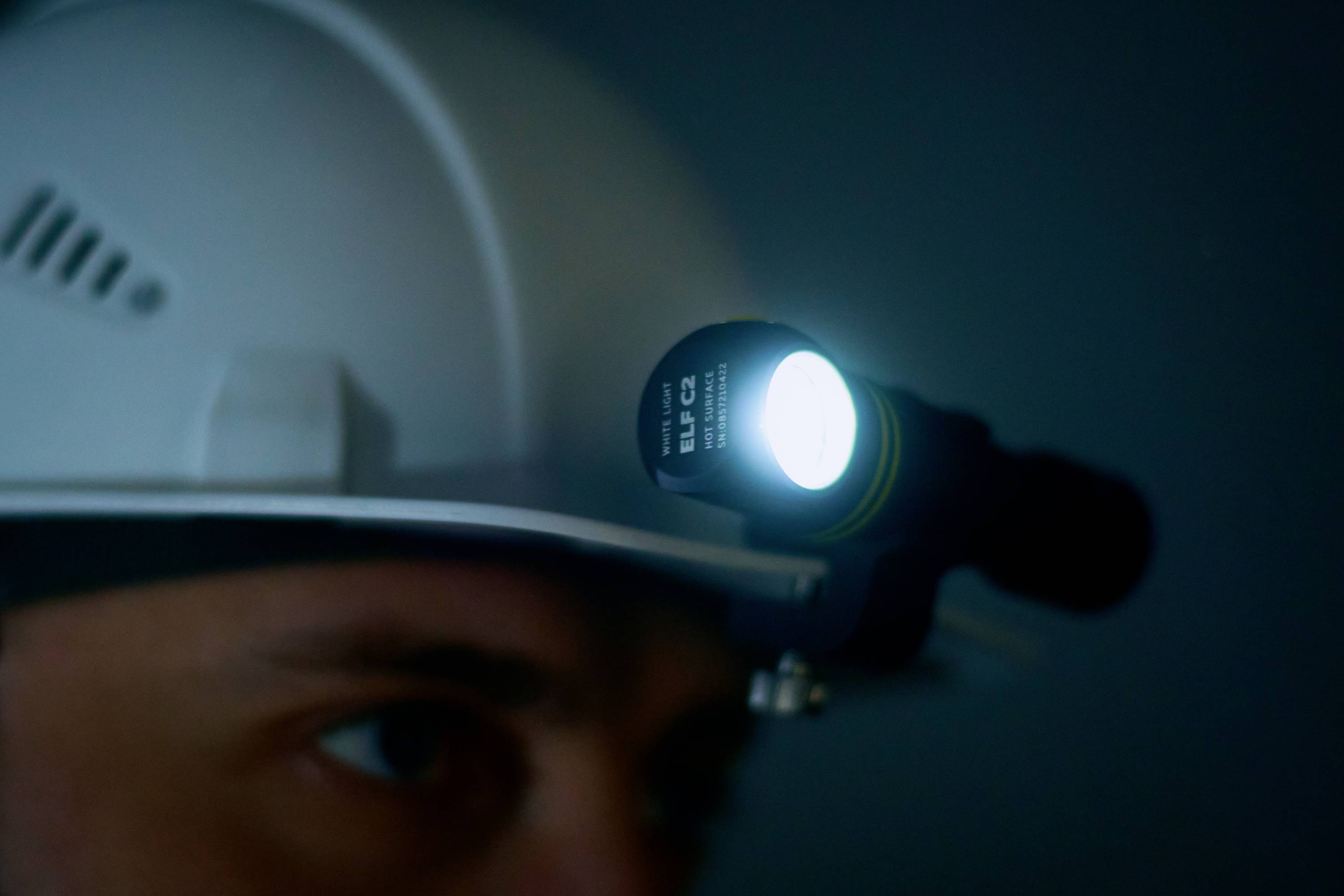 A person is wearing a safety helmet with a bright head torch in a dark room, indicating work in a dark environment.