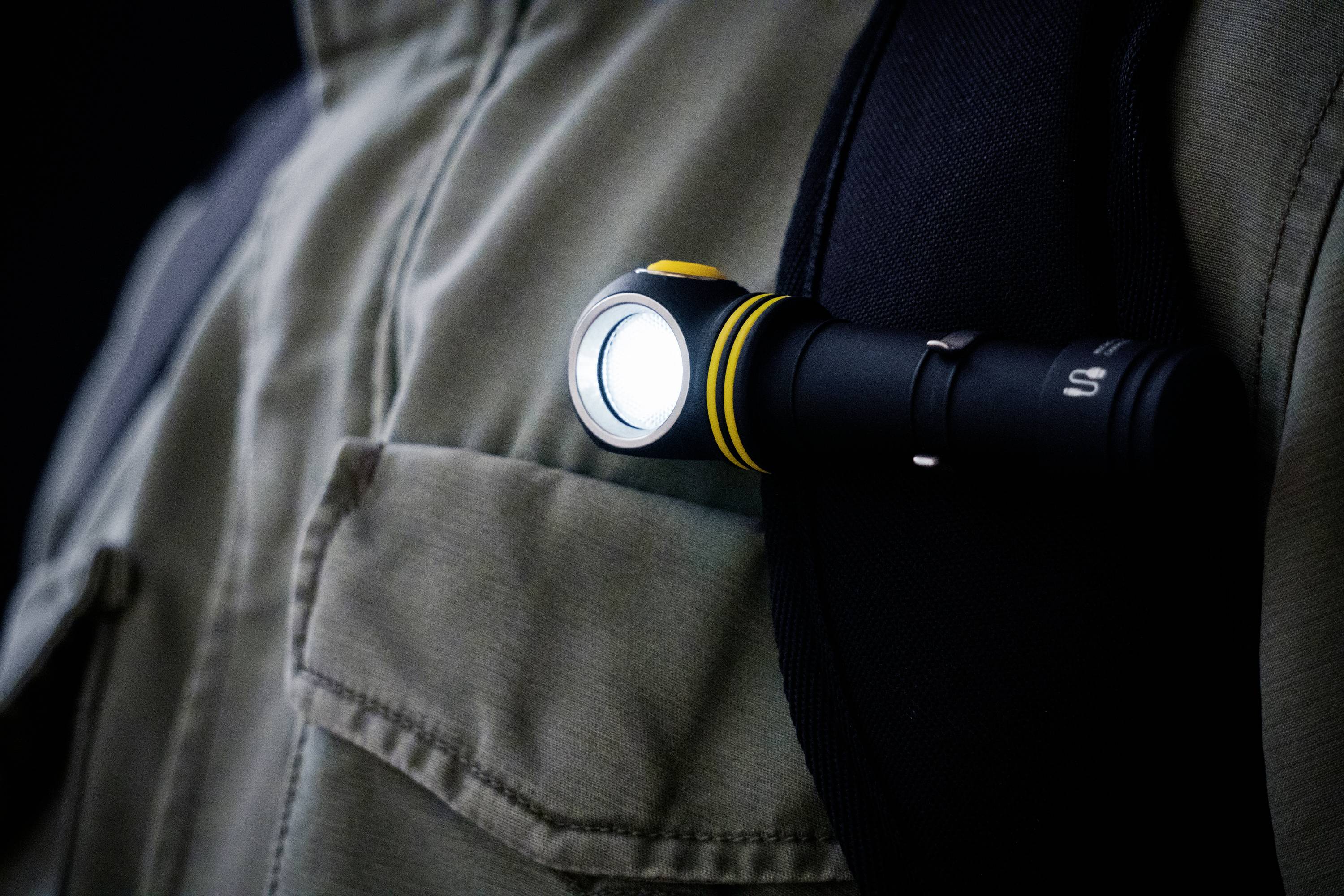 A torch is attached to a rucksack strap, shining brightly and providing illumination when walking in the dark.