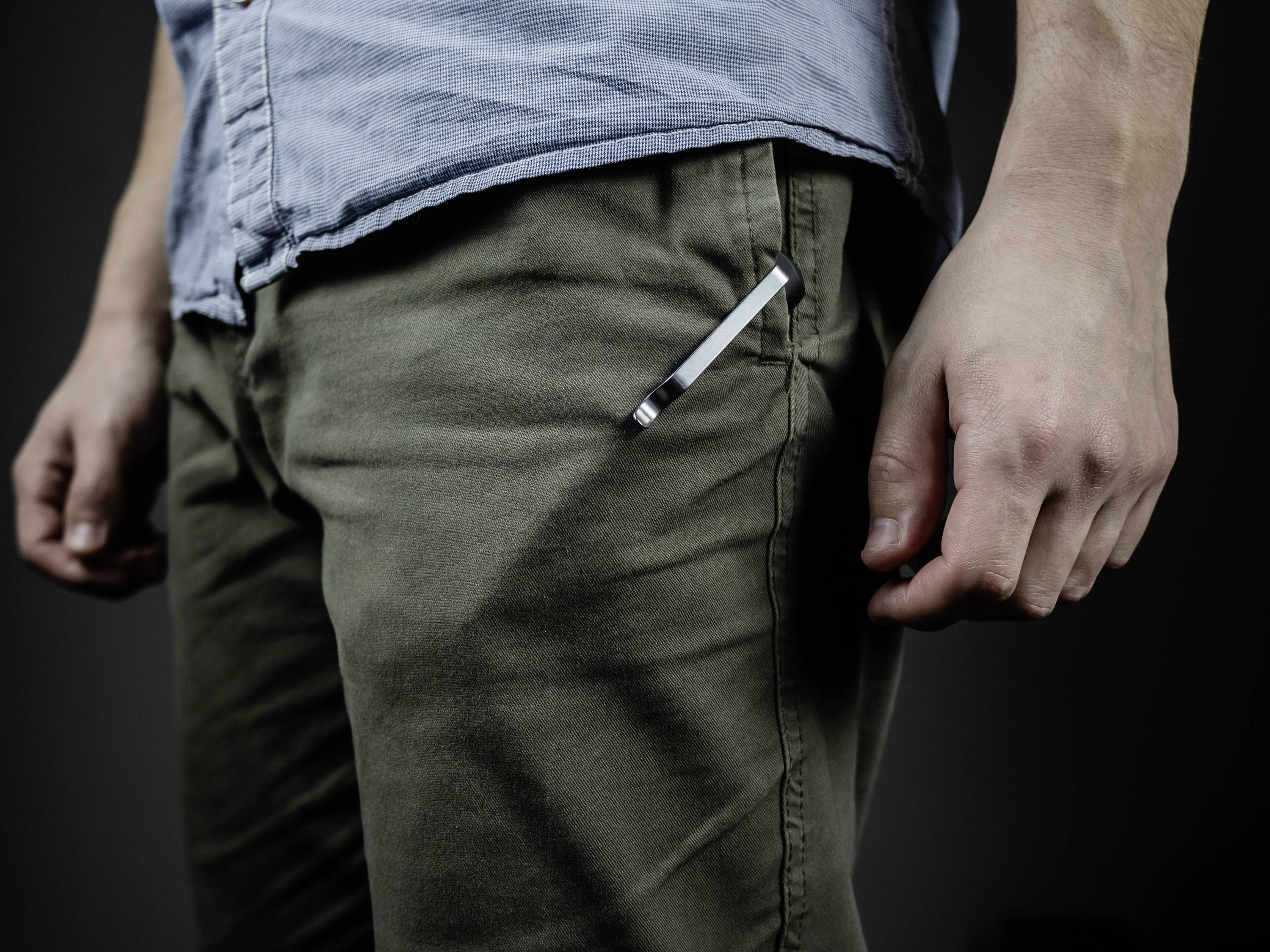 A man is wearing a blue shirt and green trousers. A pen is tucked into the trouser pocket. The focus is on the lower half of the body.