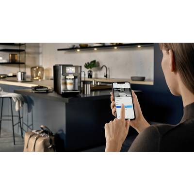A person is controlling a coffee machine in a modern kitchen via a smartphone app. The machine is preparing a coffee.