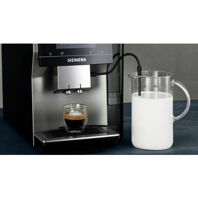 A coffee machine is making an espresso in a glass. Next to it stands a glass jug of milk with an attached milk tube.