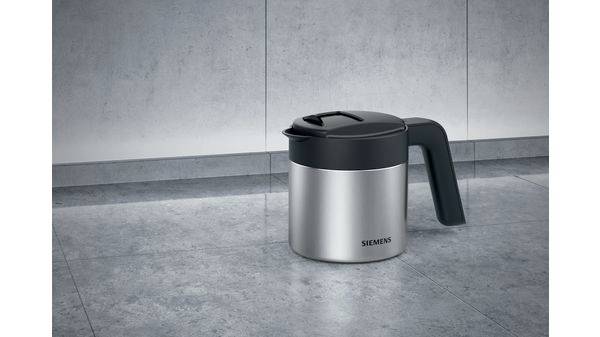 A silver teapot with a black handle and lid is sitting on a grey stone floor.