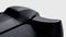 Close-up of a black game controller trigger with a textured grip and visible 'R1' markings, against a grey background.