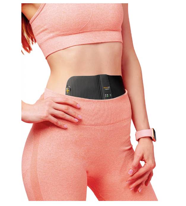 A woman is wearing a modern fitness device on her abdomen. She is dressed in a pink sportswear. The focus is on the device for abdominal muscles.