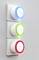 'Three circular light switches stacked vertically on the wall, glowing in blue, green, and red, with the text 'me' in the centre.'