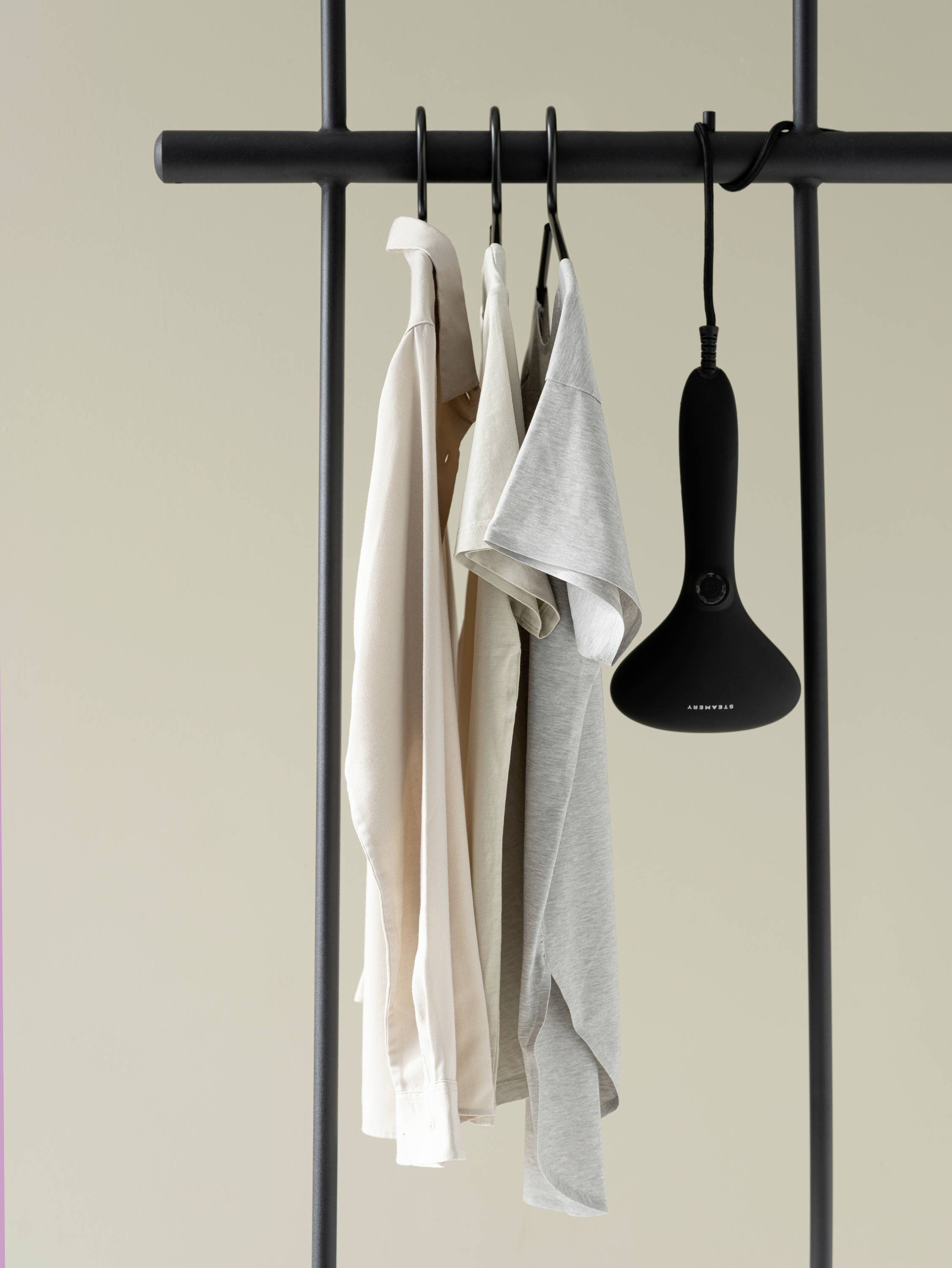 Three shirts in different colours hang on a clothes rail next to a black steam iron.