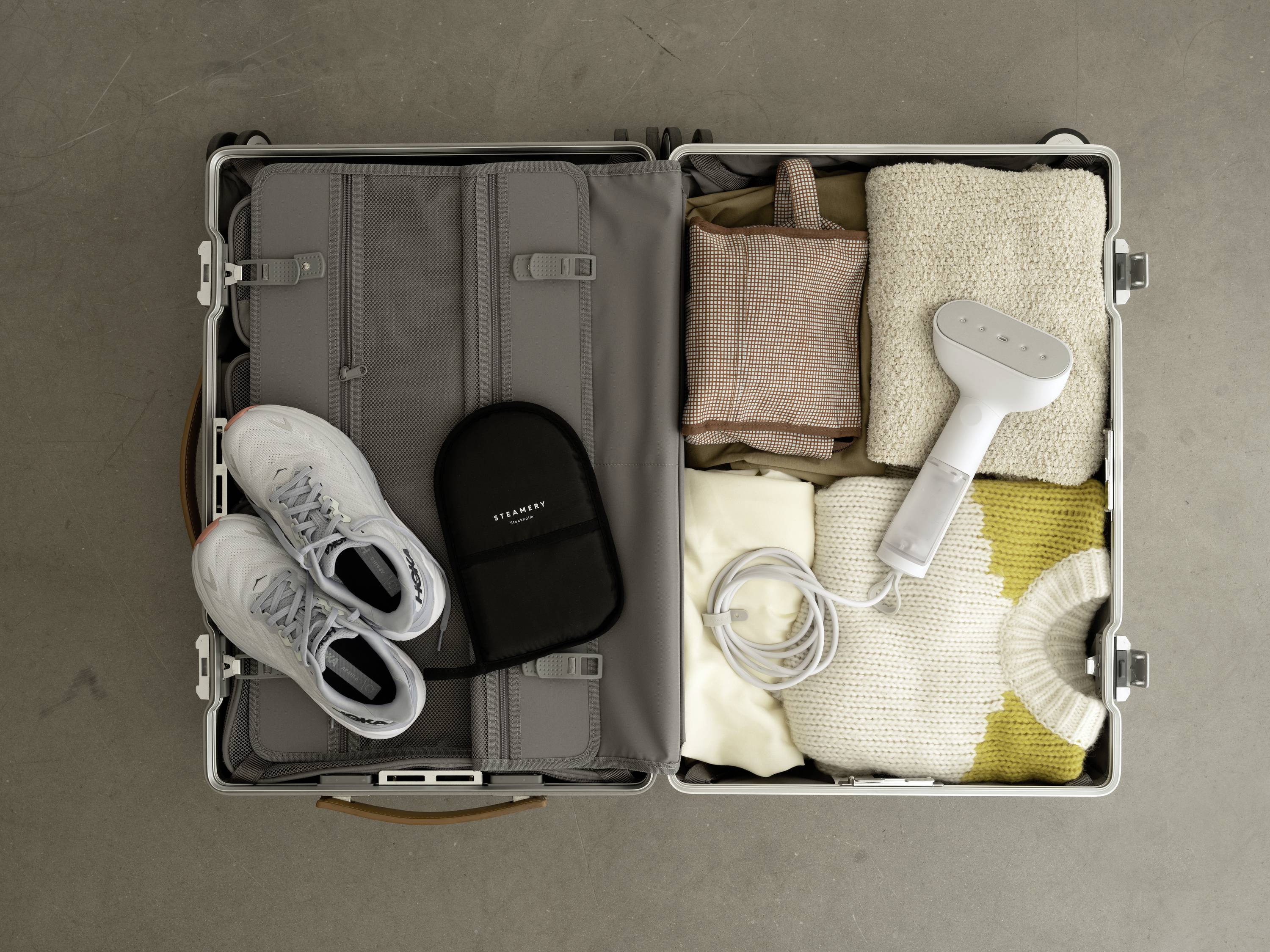 An open suitcase contains clothing, a pair of shoes, a travel adaptor and a portable steam iron. Ideal for travelling.