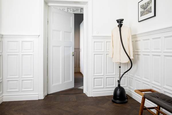 Open door in a room with light wallpaper. A steam generator on a wooden chair, a picture on the wall. Cosy living atmosphere.