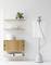 A clothes steamer is pressing a white shirt. Next to it stands a shelf with minimalist decoration and plants.