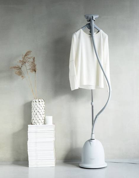 'Steam iron with white top against a grey background, next to a stack of magazines with a decorative vase.'
