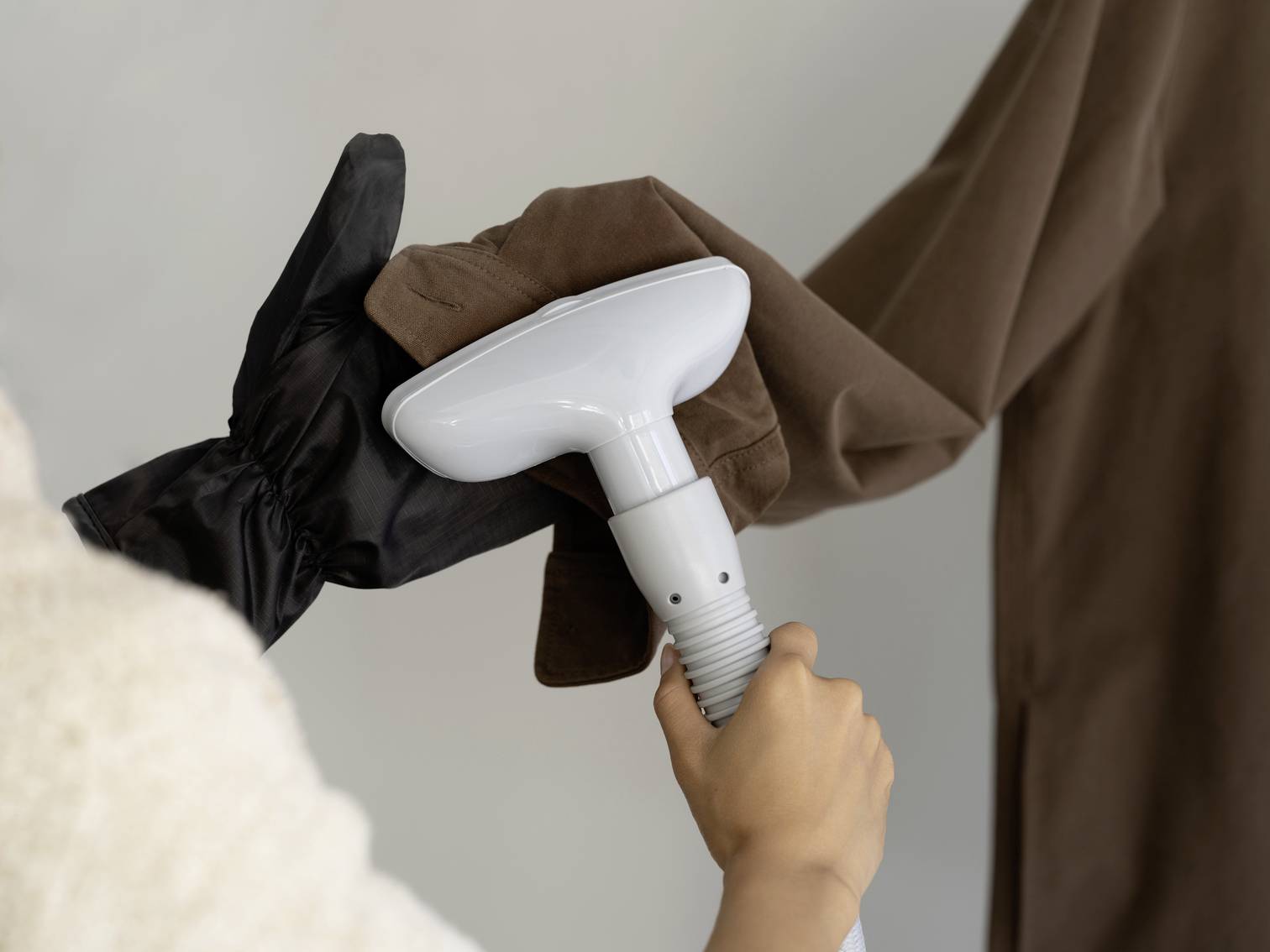 Someone is steam ironing a brown garment with a hand steamer. One hand is wearing a black protective glove.