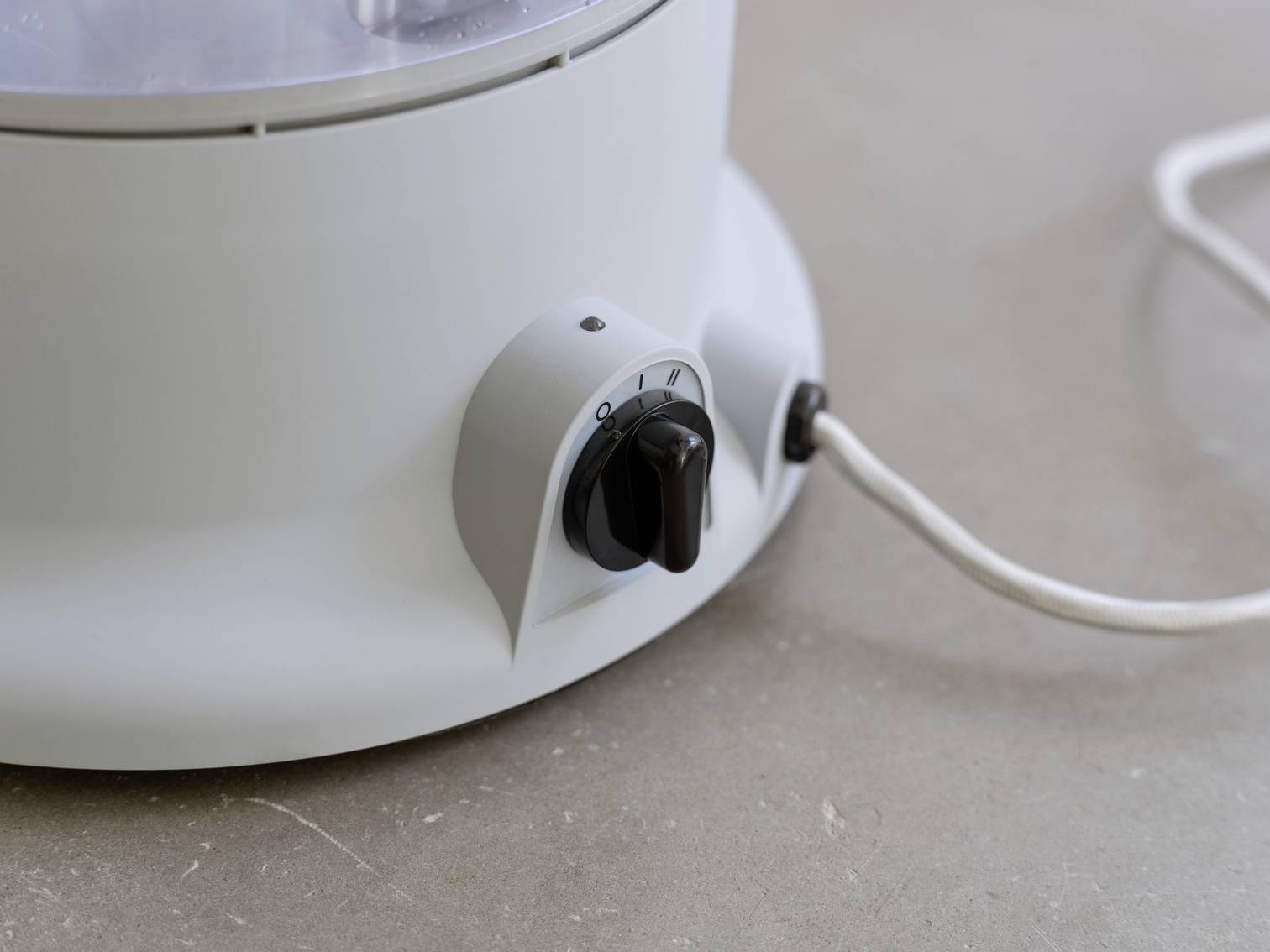 A white kitchen appliance with a black rotary knob for adjusting the power level, placed on a grey surface.