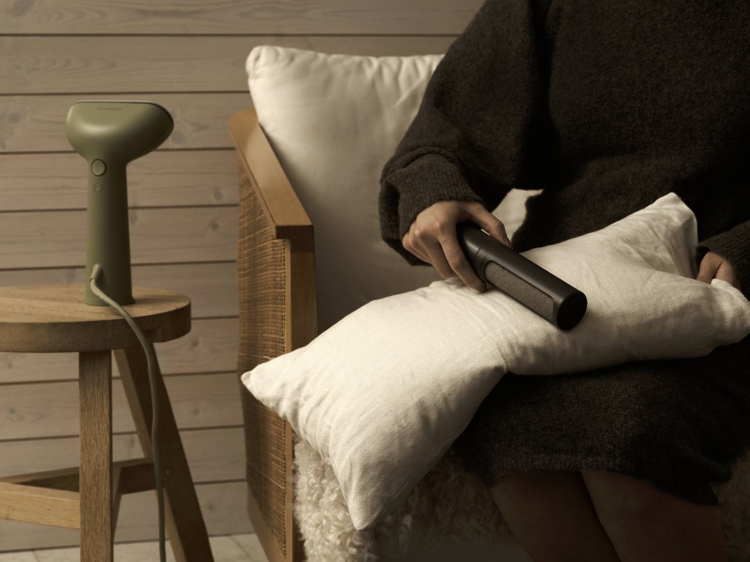 A seated person is using a handheld device on a white cushion, with an office device placed on a wooden stool beside them.