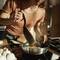 A woman is cooking in the kitchen and stirring with a black wooden spoon in a pot on the hob. Sunlight is streaming into the room.