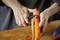 A person is peeling a carrot with a vegetable peeler on a wooden chopping board. Hands and utensil are in focus, with a kitchen activity clearly visible.