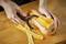 A person is peeling a butternut squash with a vegetable peeler on a wooden chopping board. Peel strips are lying beside it.