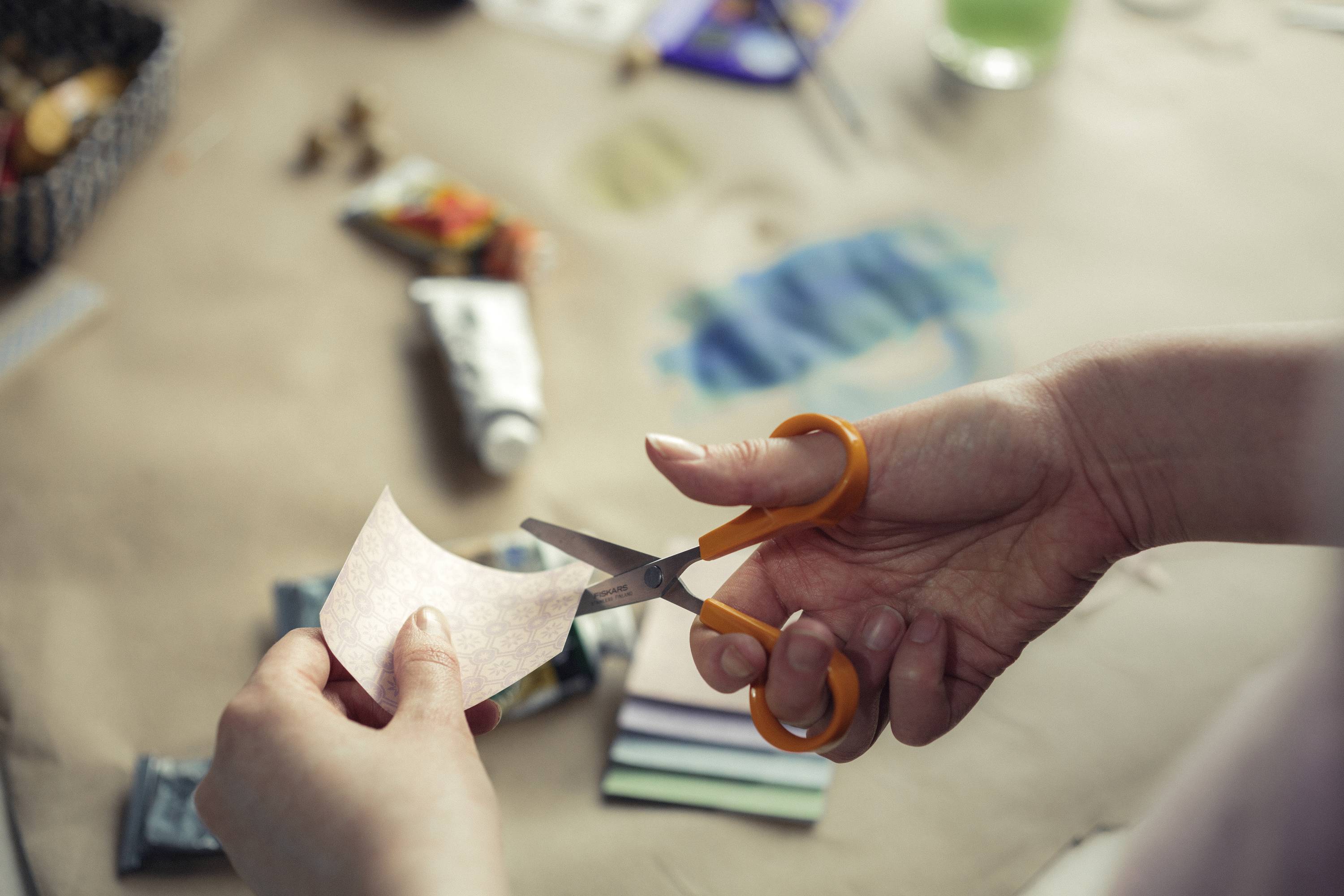 A person is cutting a small piece of paper with scissors on a table full of art materials.