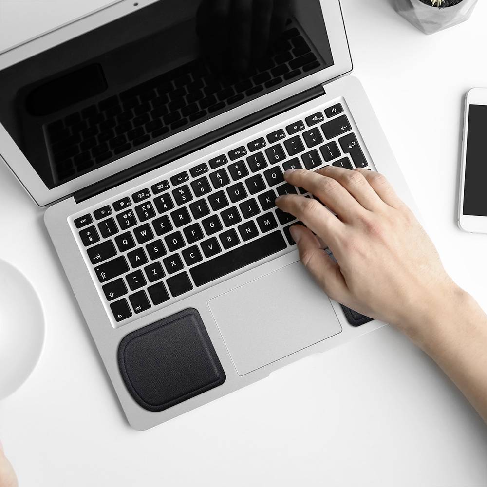 A person is typing on a laptop with a reflective screen. They are holding a white coffee mug in their hand.