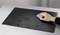 A hand wipes water droplets from a black, rectangular surface on a grey table with a grey cloth.