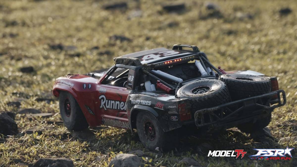 Remote-controlled model car with 'Runner' inscription drives over grass and stones. No further details are discernible in the background.
