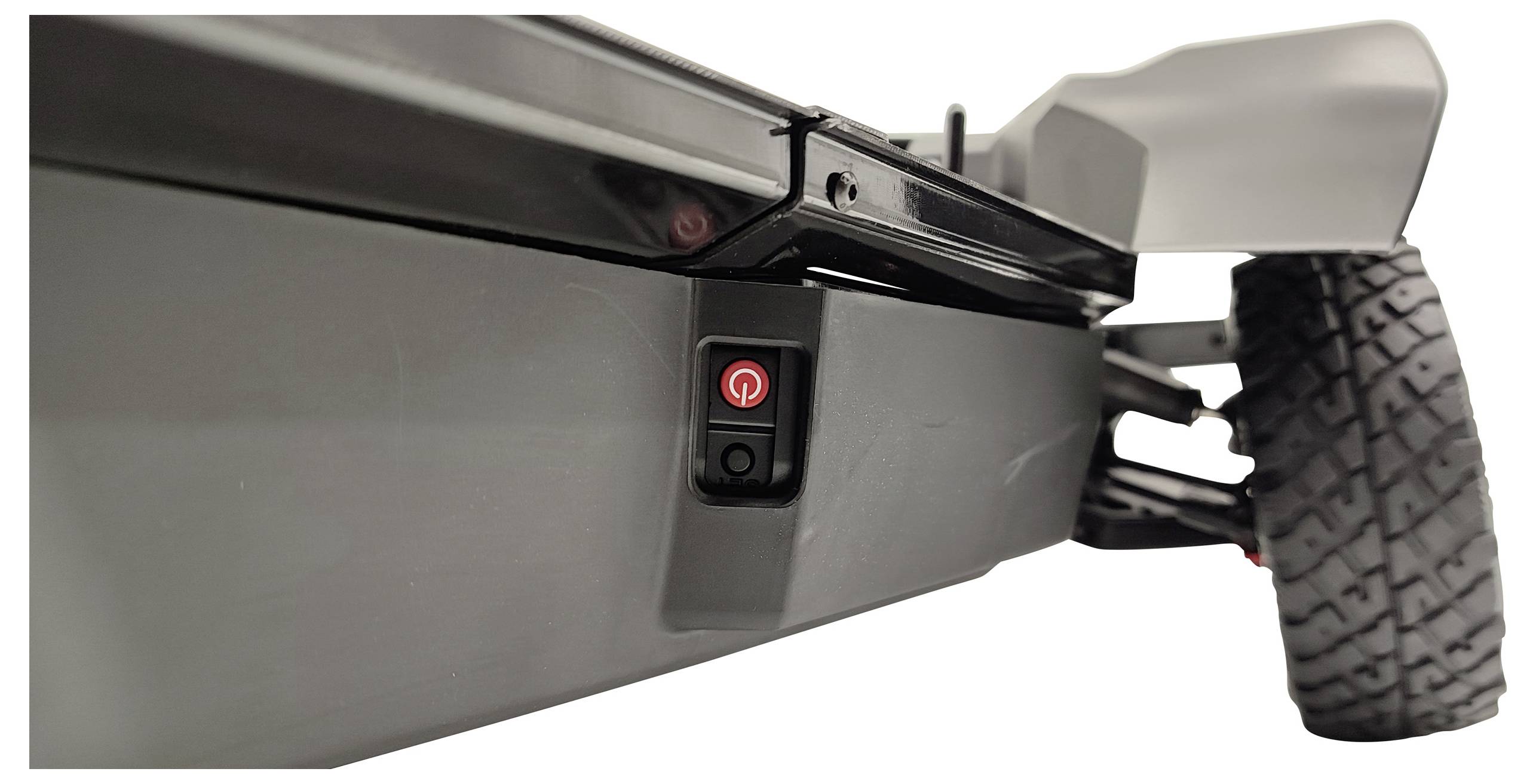 Underside of a lawnmower with a red on/off switch. One wheel and part of the casing are visible.