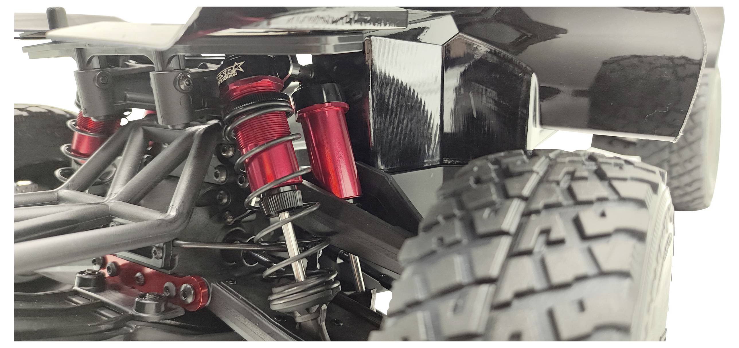 Close-up of the chassis of a remote-controlled car with a red shock absorber and chunky tyre. Focus on suspension and details.