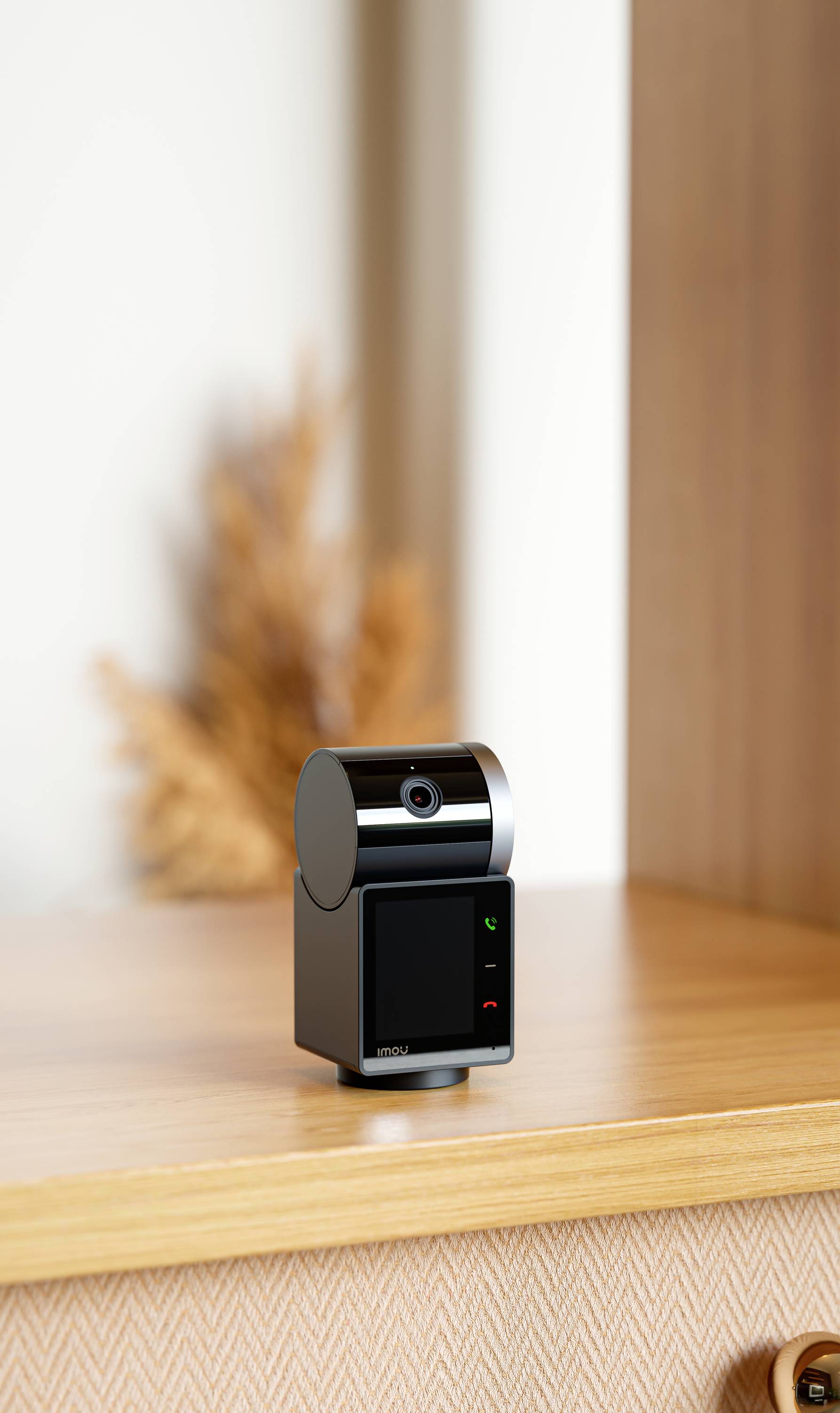 A compact, black surveillance camera on a wooden table; blurred brown decor is visible in the background.