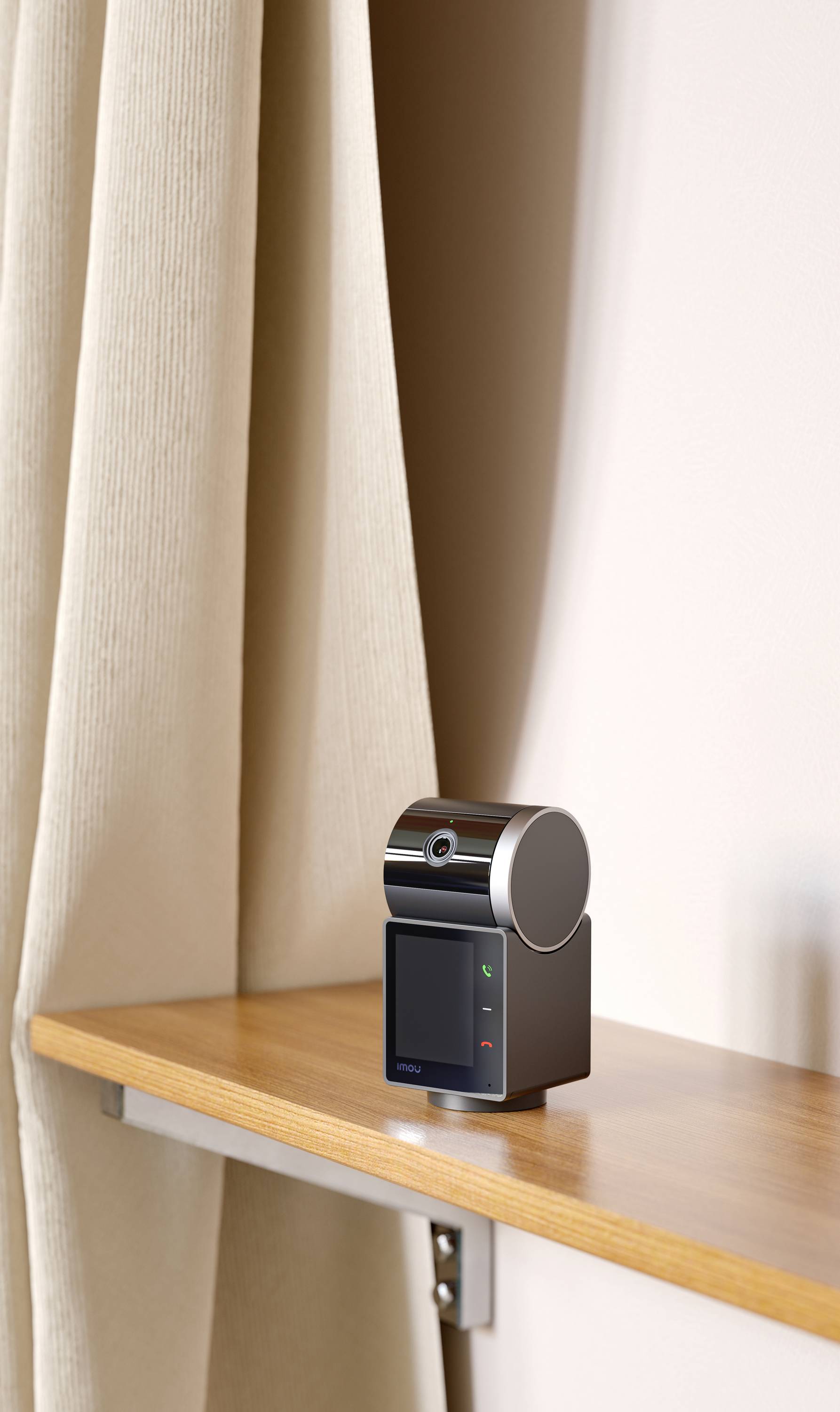 A small, modern device with a round head and display sits on a shelf in front of a beige curtain.