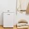 A Bosch air purifier stands on the floor next to a stack of beige towels and a hanging cardigan.