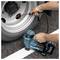 A person inflates a vehicle tire using a Makita portable air compressor on a road. The compressor displays '40V max' branding.