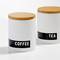 Two white storage containers with wooden lids, labelled 'COFFEE' and 'TEA'. They are positioned side by side on a white surface.