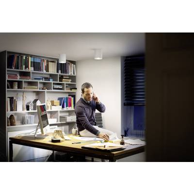 A man is sitting at a desk in a modern office, talking on the phone and checking documents. Bookshelves with books are in the background.