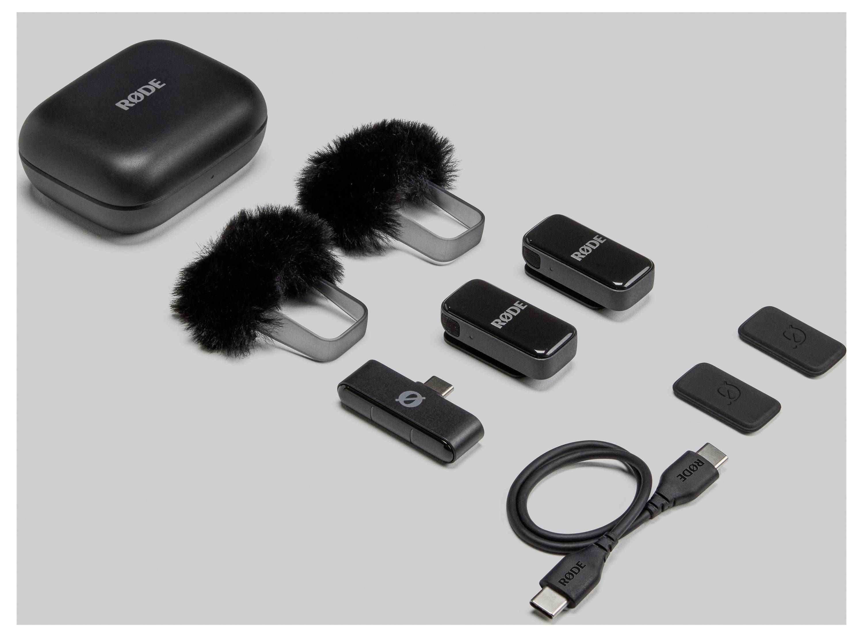 'Top-down view of a complete wireless microphone system with charging case, microphones, windshield, receiver, cable and adapter on a grey background.'