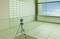 'Laser measuring device on tripod is aligning itself in an empty room. White grid lines on the wall, blue window with cloudy sky.'