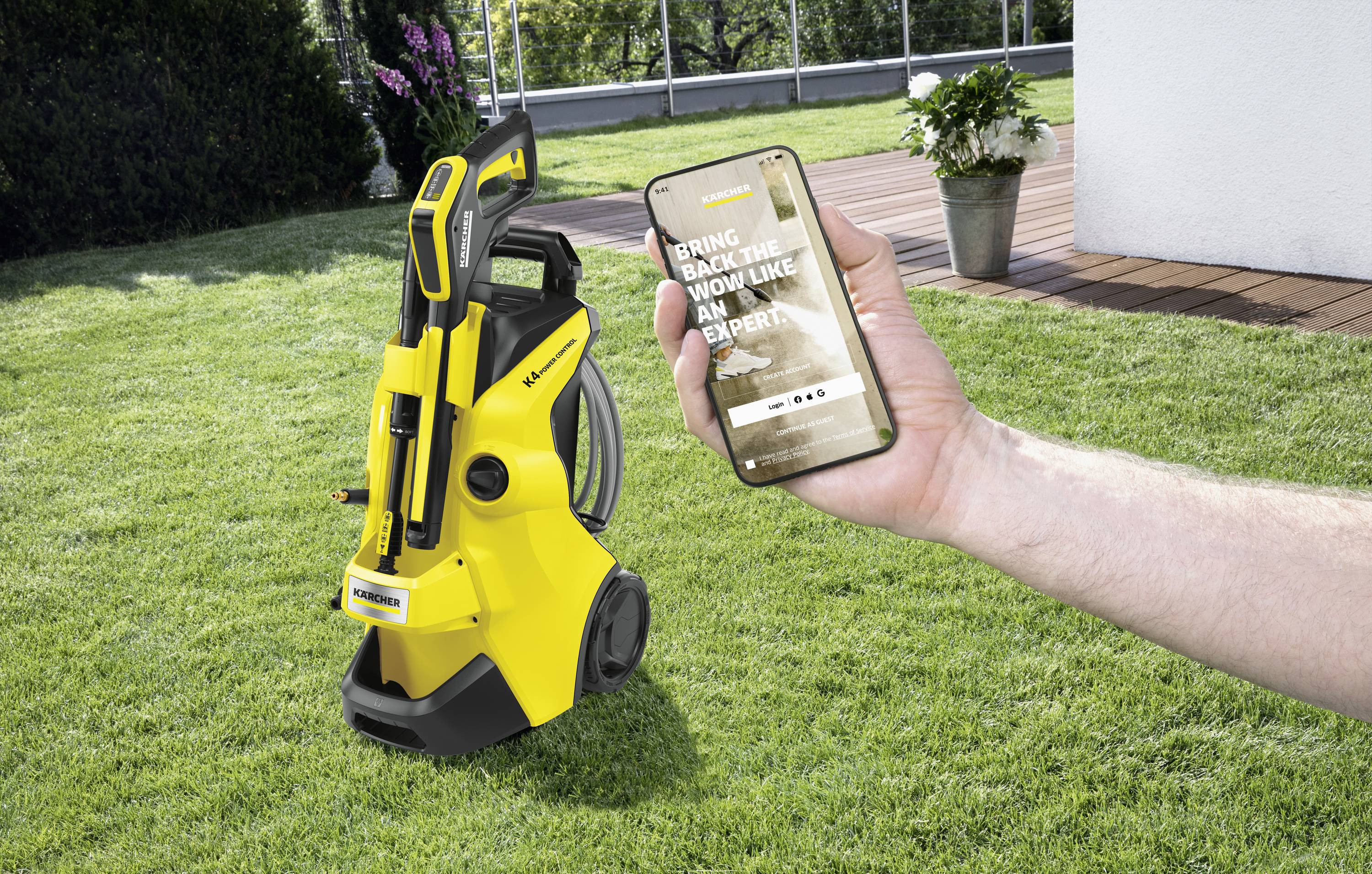A person is holding a smartphone over a well-maintained lawn. A yellow pressure washer stands in the background. The screen displays a website.