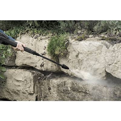 A person is cleaning a stone wall in the garden using a pressure washer.