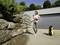 A person is cleaning a stone wall outdoors using a pressure washer. A grey garage is visible in the background.