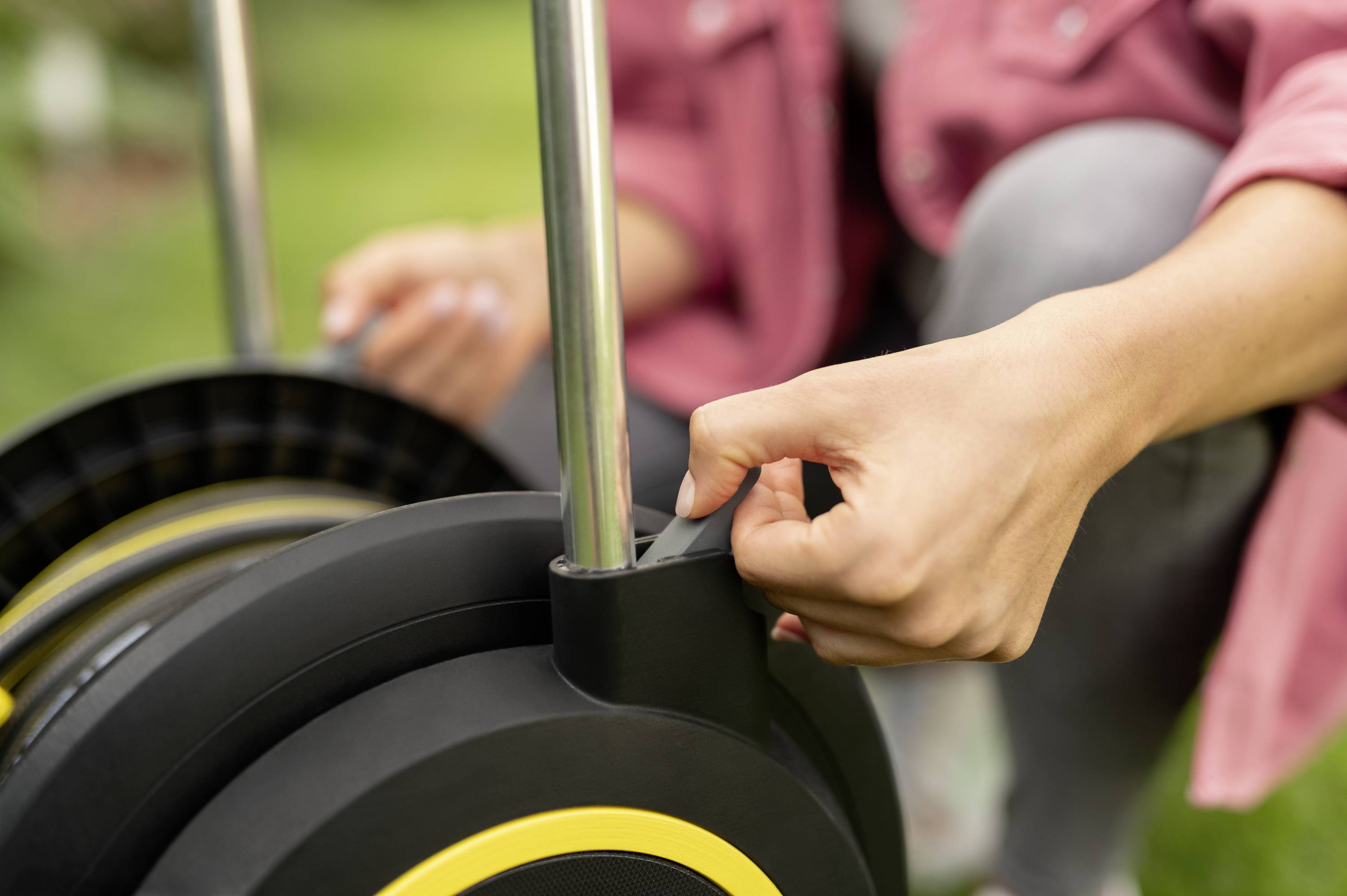 A person is attaching a hosepipe to a hose reel in the garden. Focus is on the hand gripping the handle.