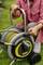 A person in the garden is holding a hose reel with a yellow hose and black wheels, ready to water the lawn.