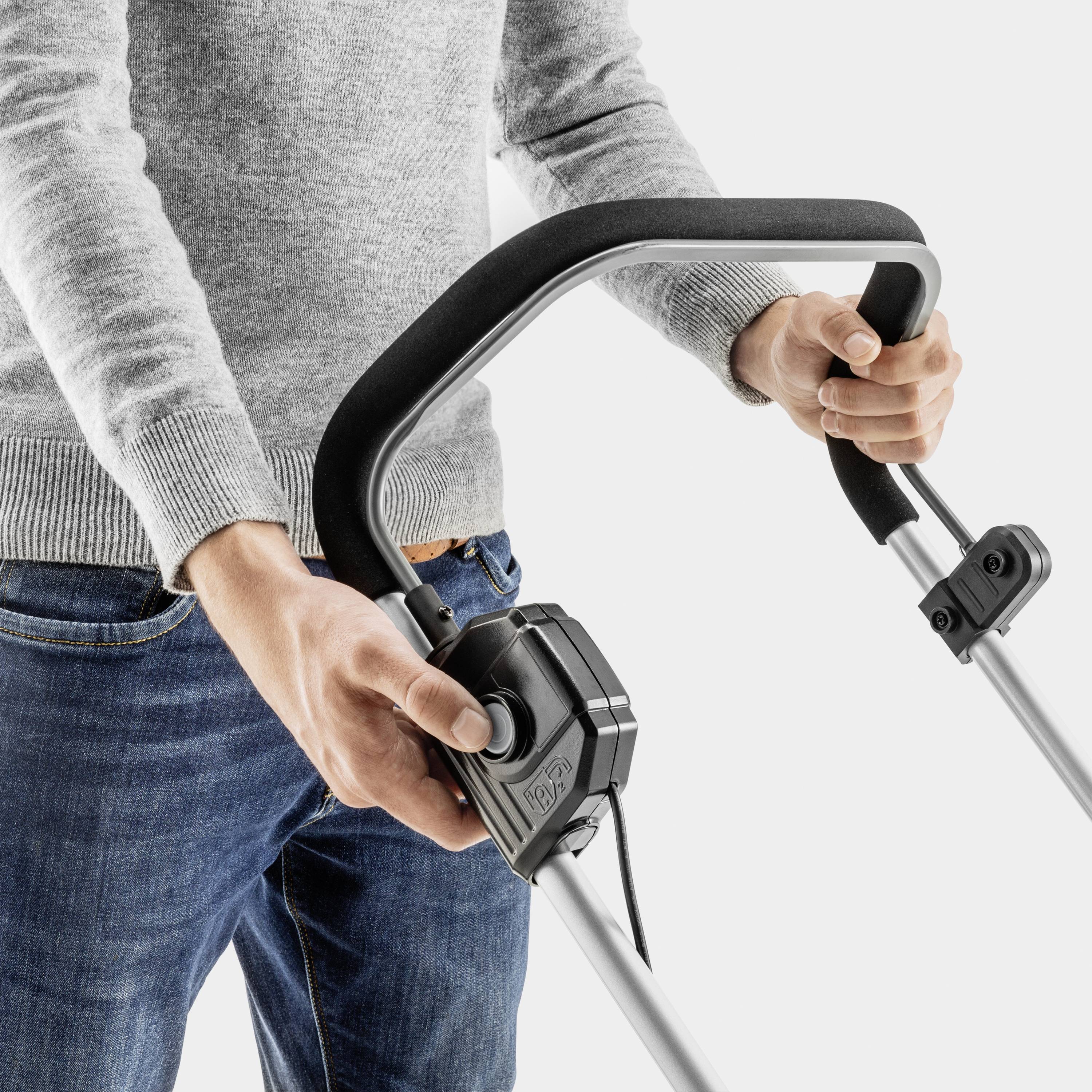 A person is holding the handle of an electric lawn mower, ready to operate. Their hands are positioned on the sturdy metal grip.